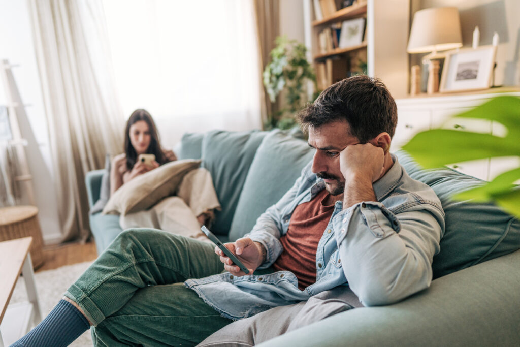 Coppia seduta insieme che fatica a comunicare mentre utilizza lo smartphone, simbolo di distanza relazionale e distrazione digitale.